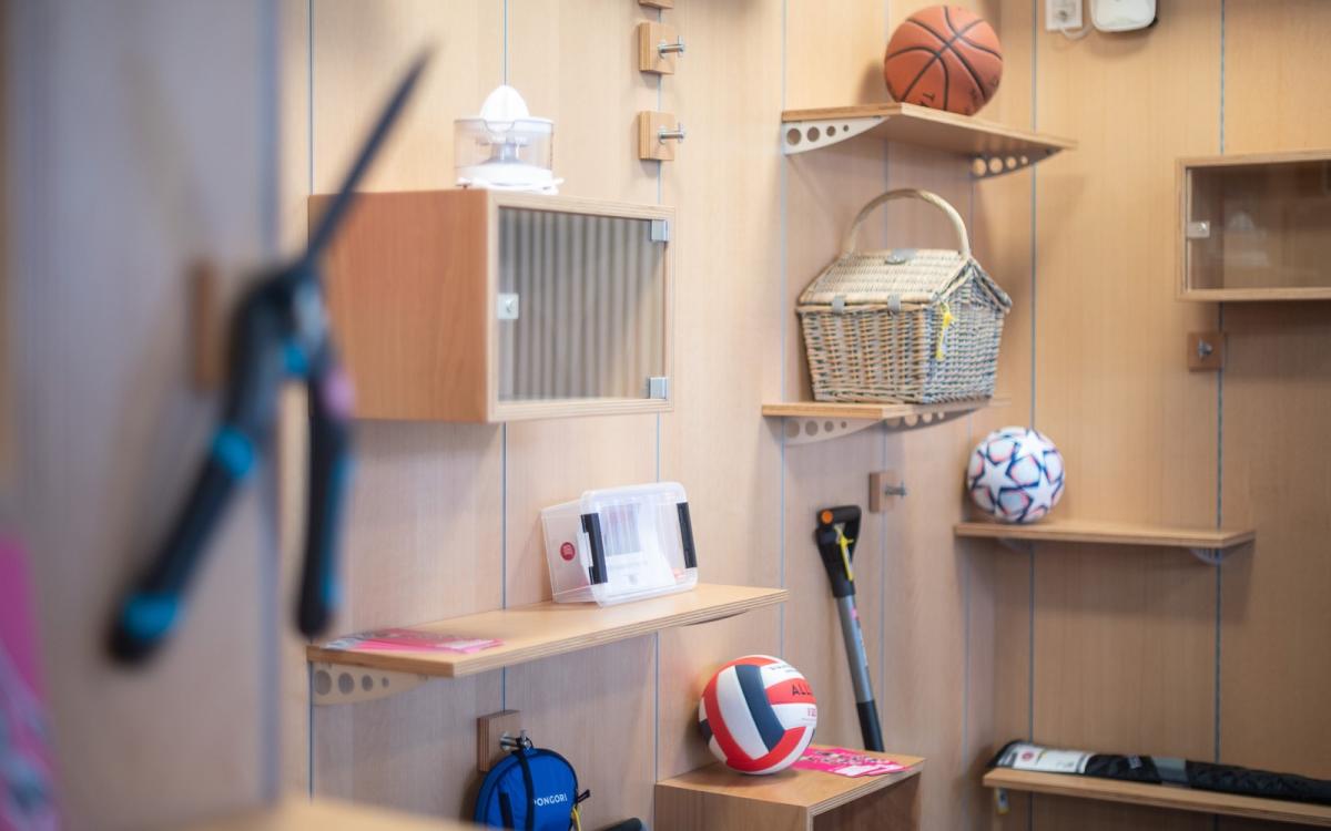 Mounted shelves on a wall display items like a picnic basket, several sports balls, and a juicer