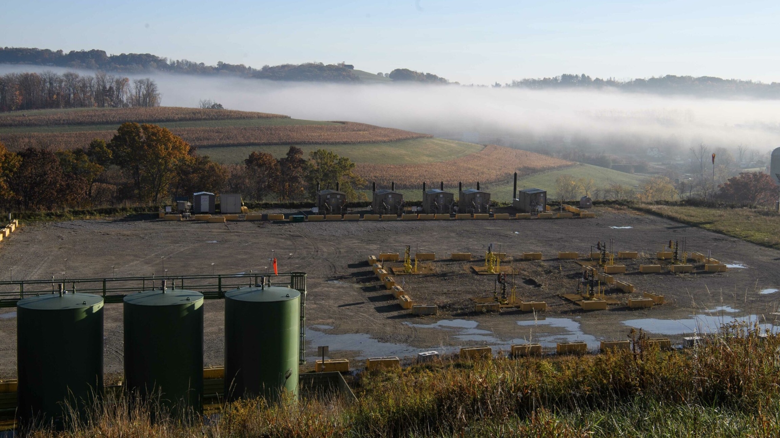 A misty field with an industrial installation on the edge.