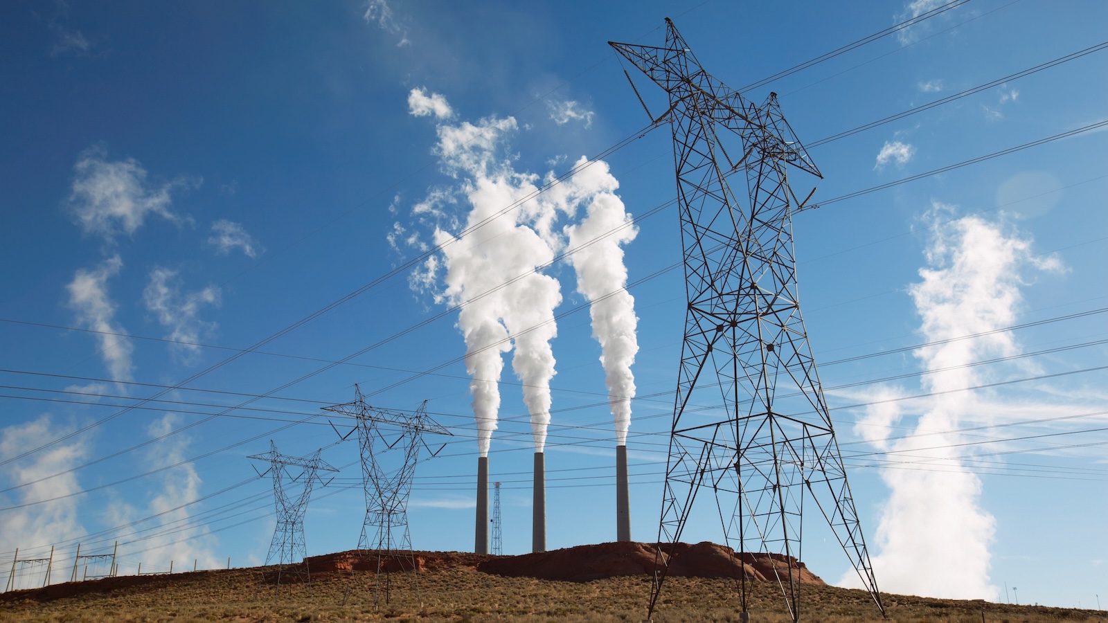 Three chimneys from a coal-fired electrical power plan send plumes of white smoke into a clear blue sky.