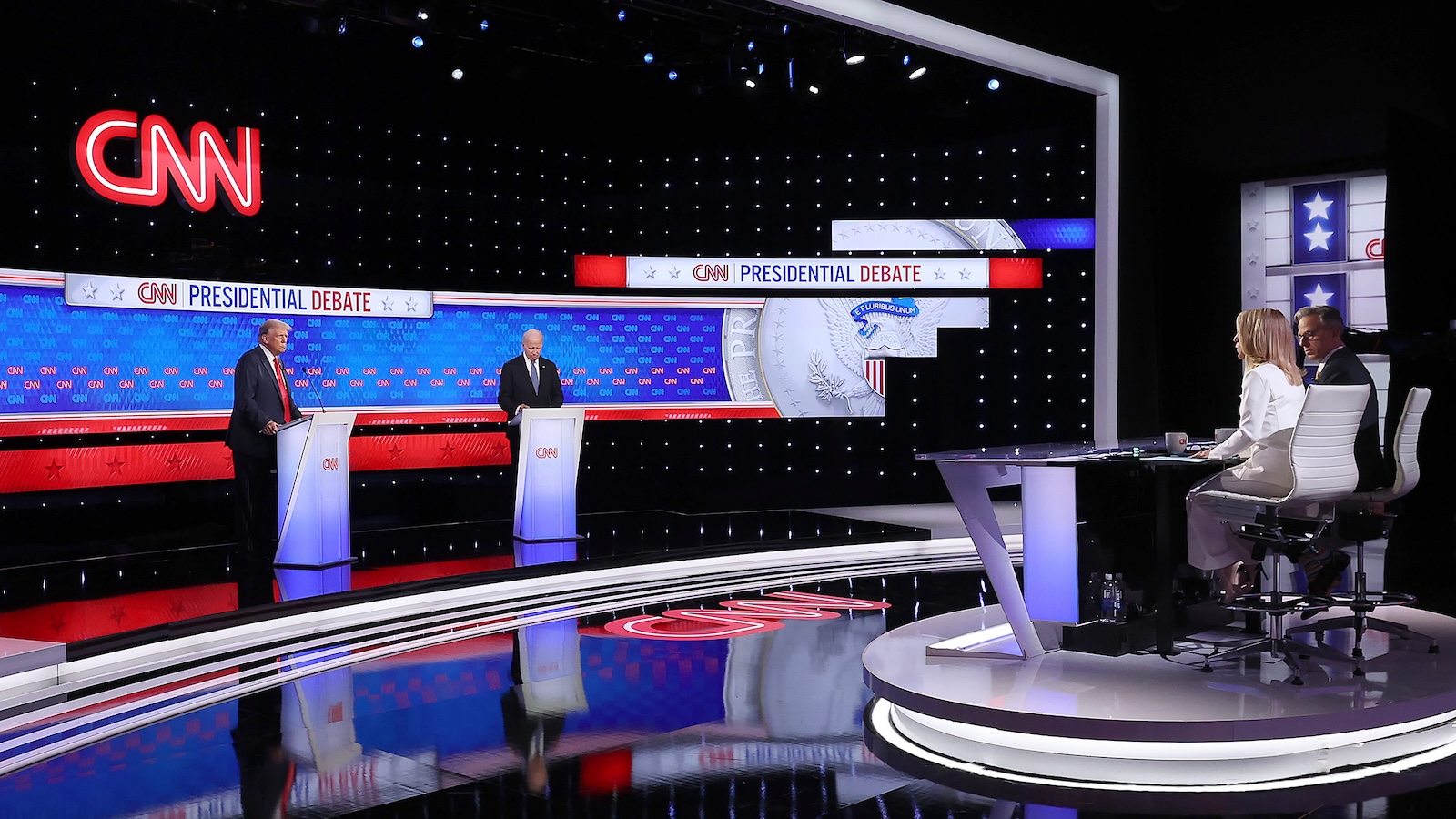 President Joe Biden and former president Donald Trump stand behind podiums on the left, and behind them is a large blue screen with the words 