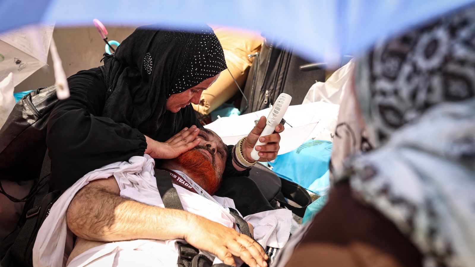 A woman uses a battery-powered fan to cool a man reeling from the scorching heat while attending the symbolic 'stoning of the devil' ritual during the annual Hajj pilgrimage.