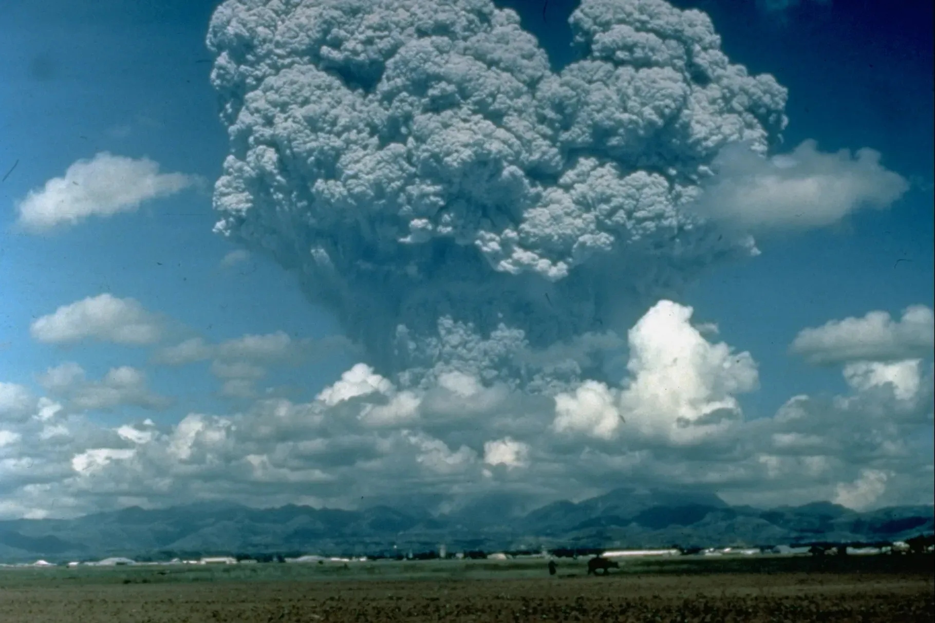 A volcano erupts, sending gray ash into the sky.