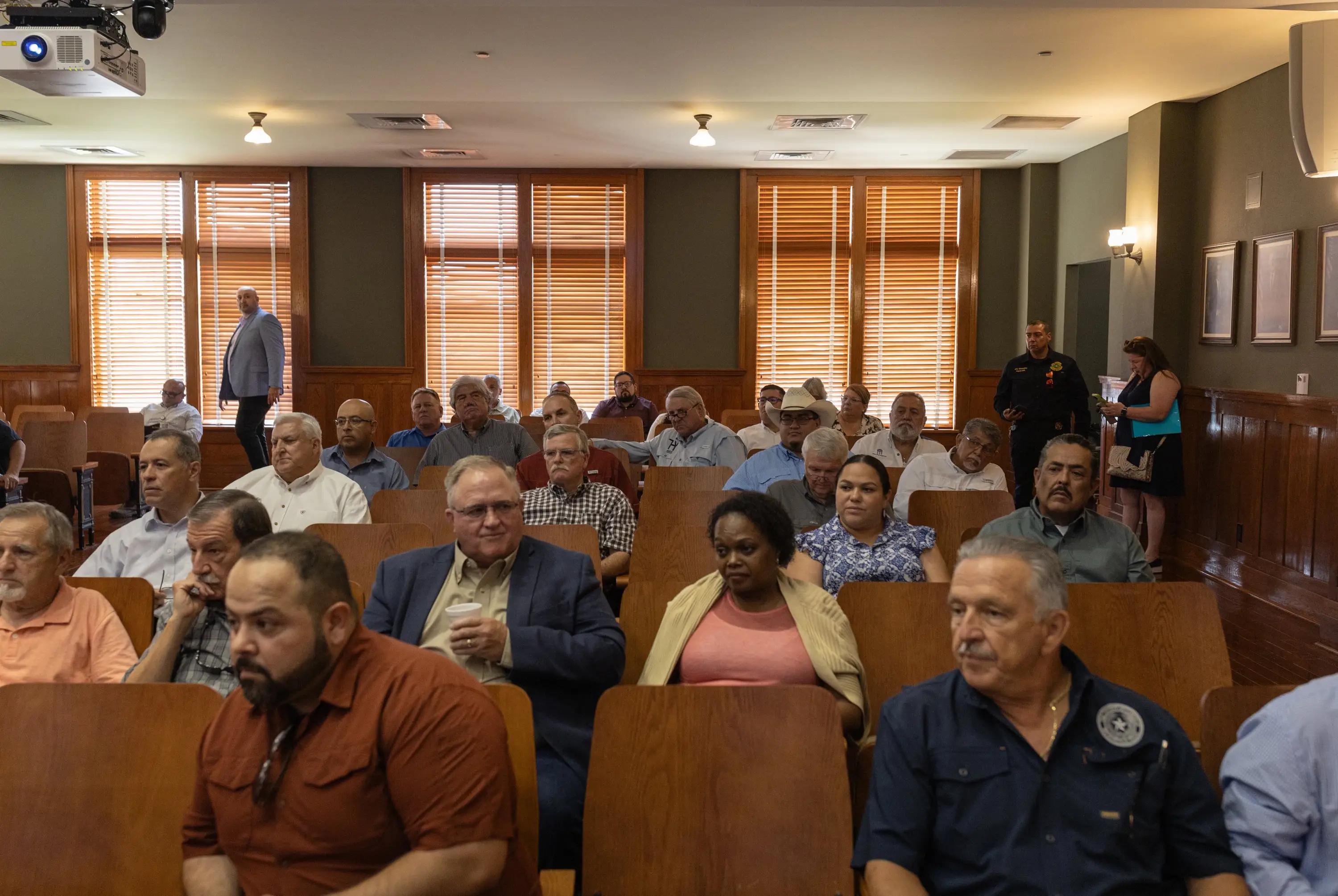 A group of people sit in a room filled with chairs.