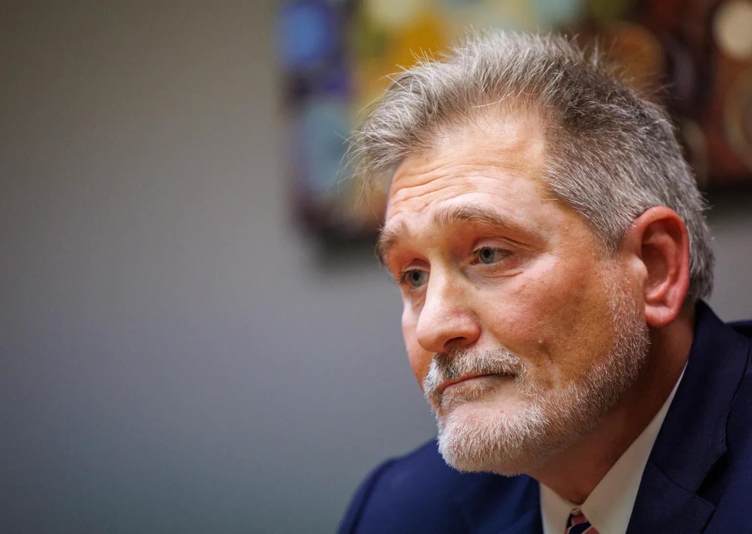 A man with gray hair and a gray beard and mustache looks wistful.