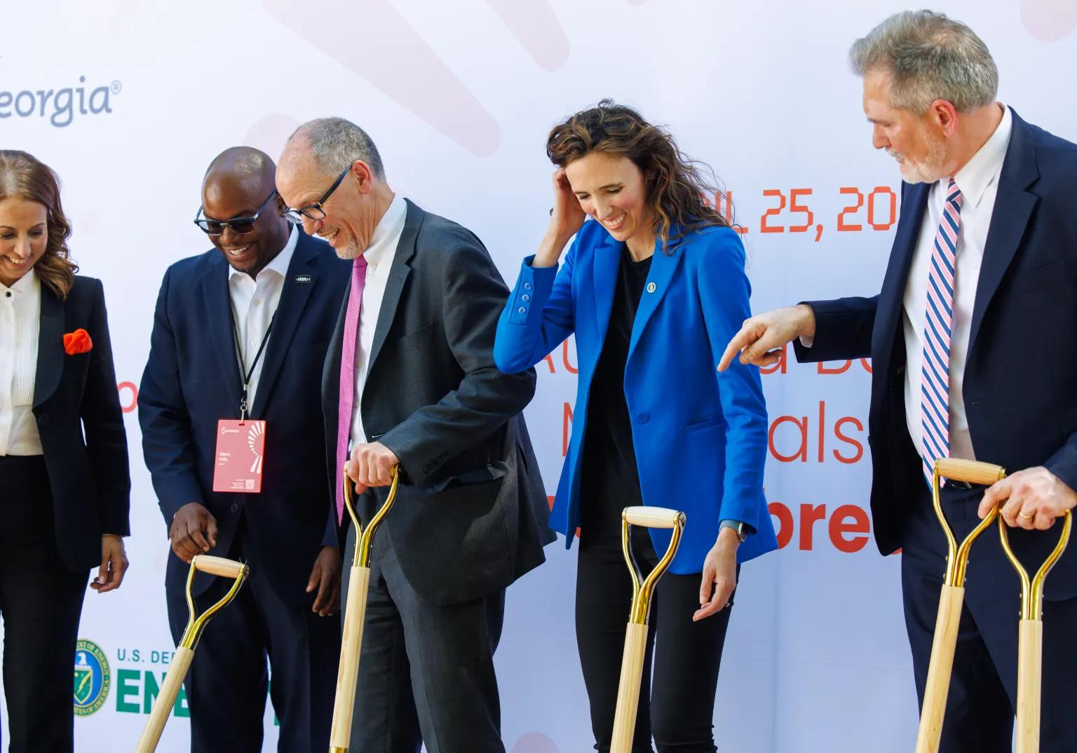 A group of people in business suits smile and hold shovels.