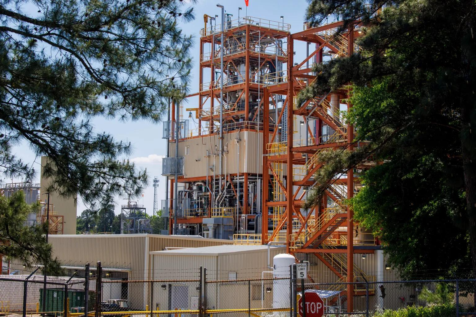 A large red industrial structure towers over trees.