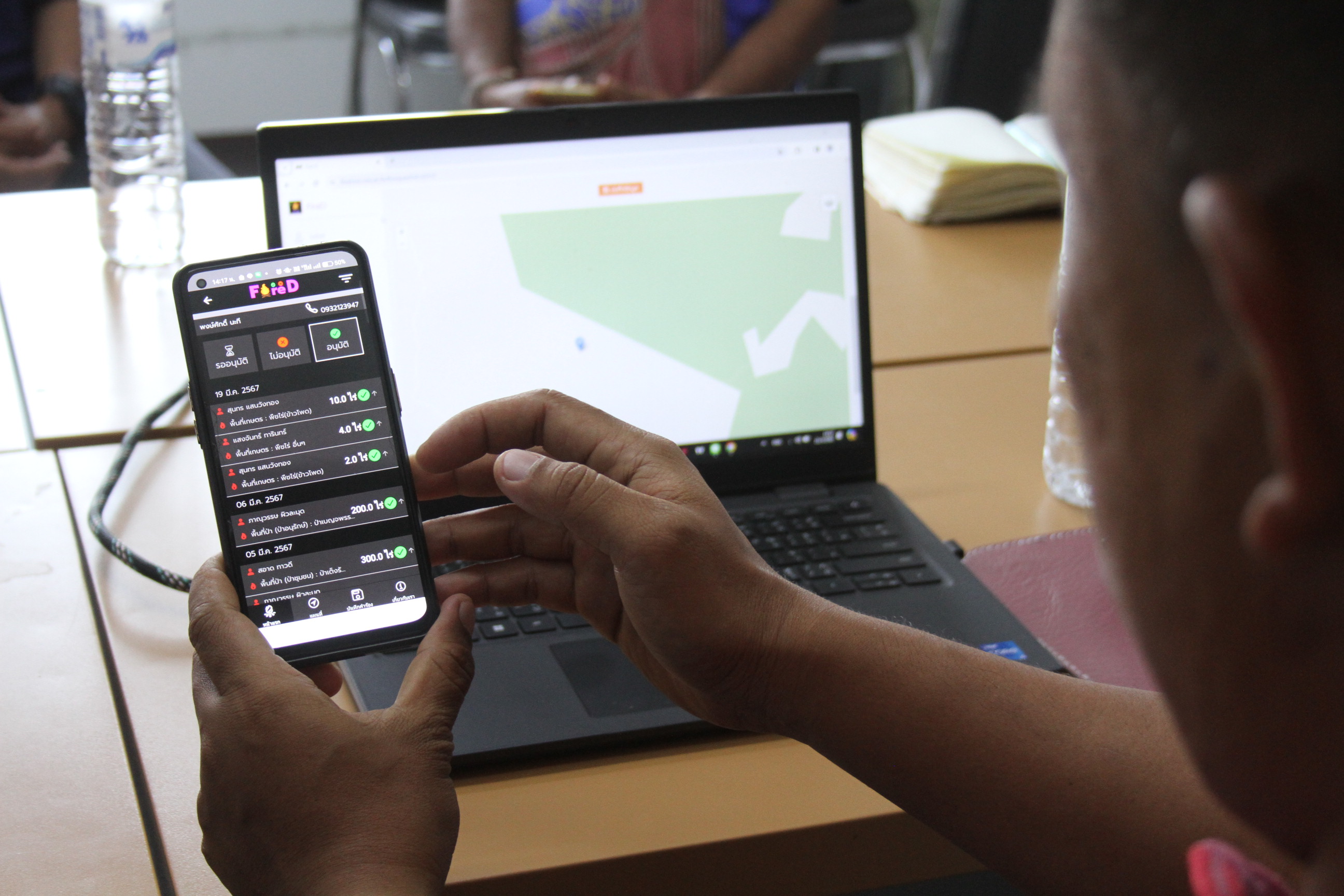 An over-the-shoulder view of a man looking at the FireD system on a phone, with an open laptop displaying a map of the area