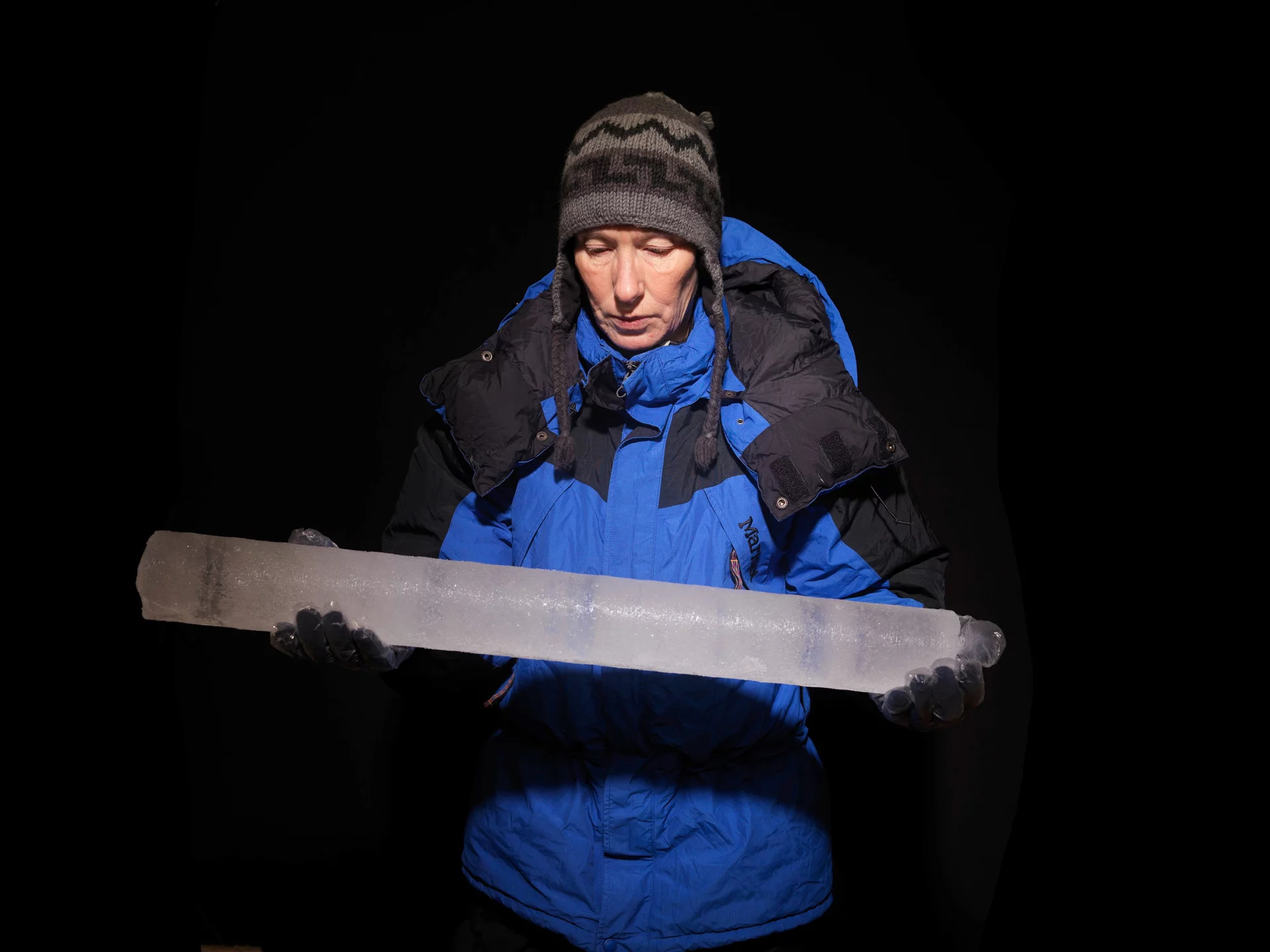 A man in a blue coat and a gray and black snow hat holds a column of ice.