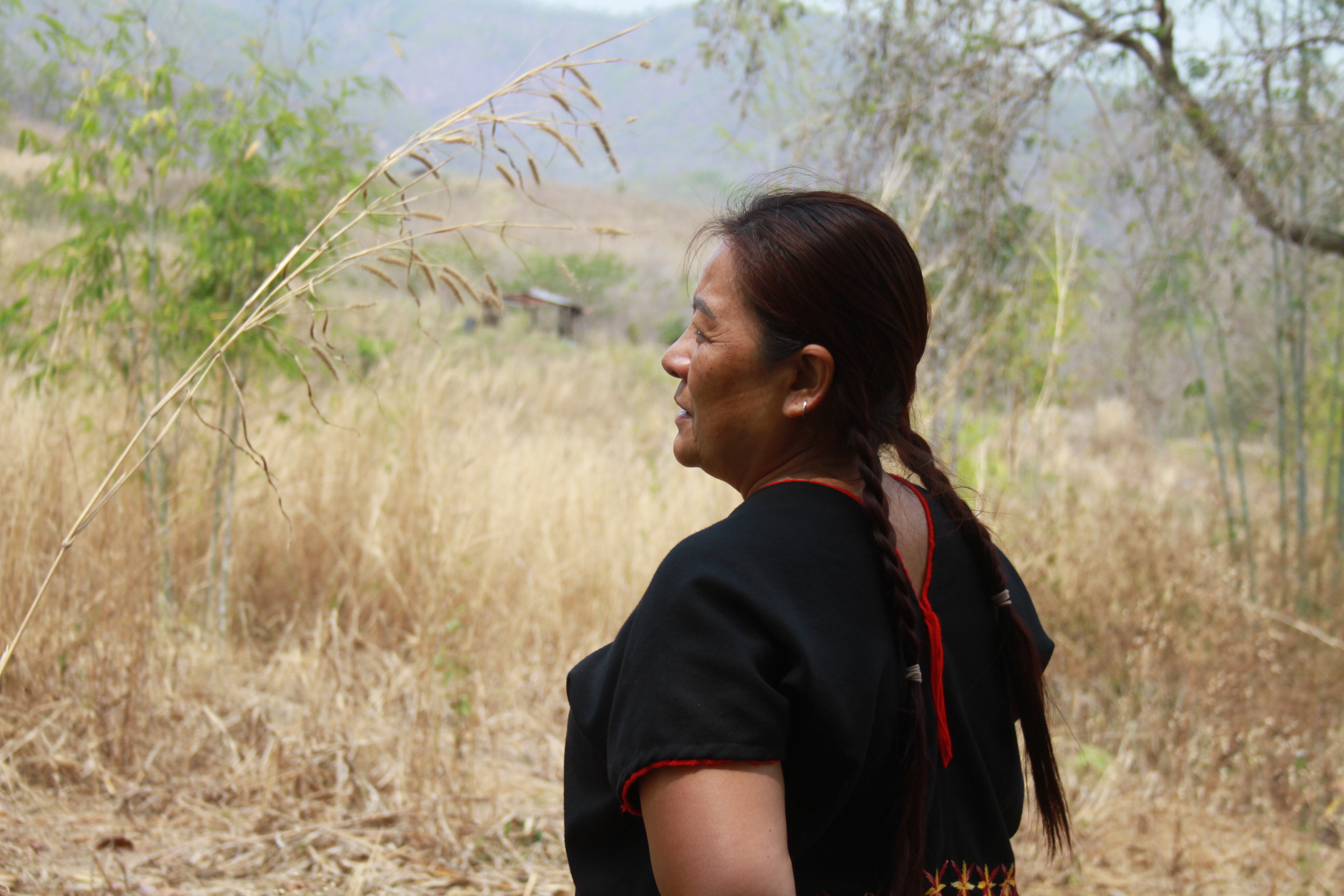 A woman stands in profile on a dry yellow field with mountains in the distance