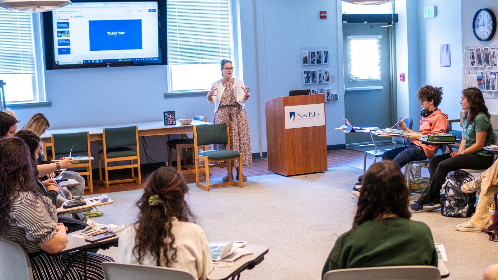 A woman stands in front of a classroom full of university students.