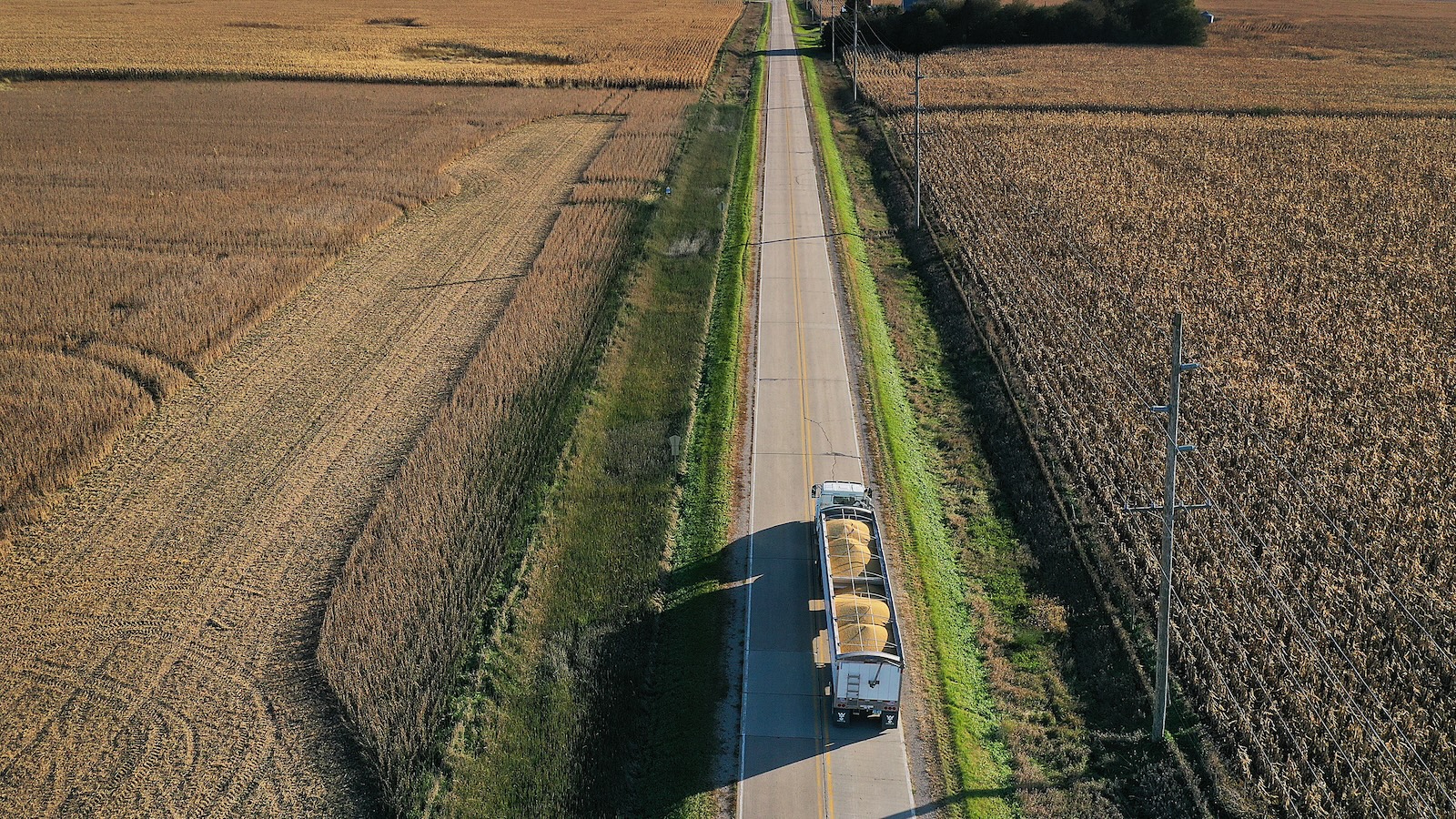 Aerial view of a large truck hauling two large containers of soybeans down a rural two-lane road with cropland on either side