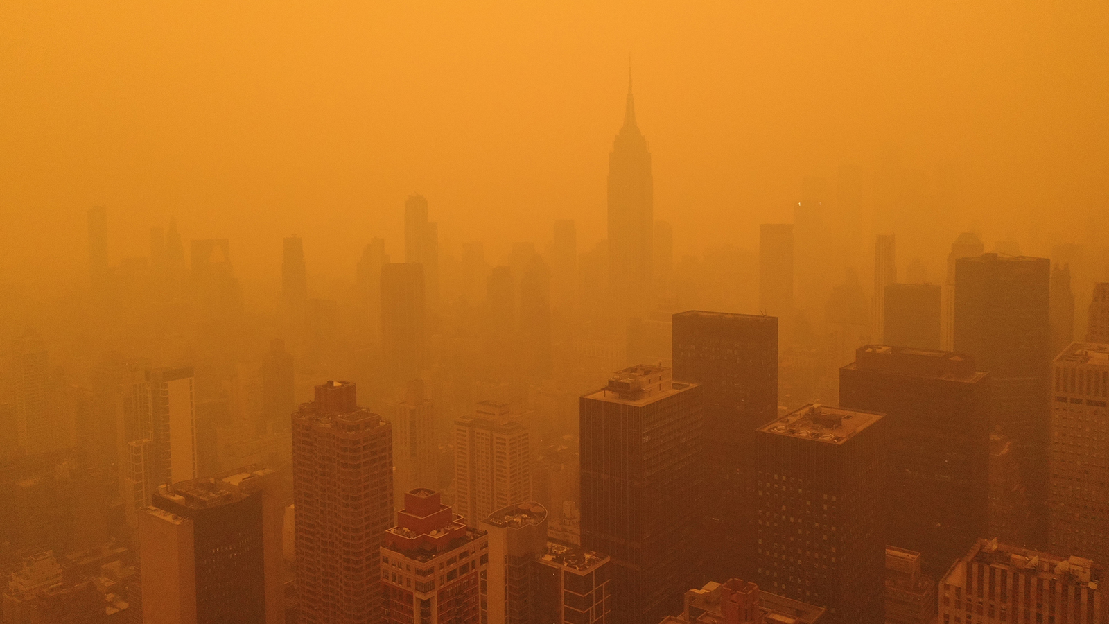 the silhouettes of sky scrapers are barely visible against an orange backdrop of smokey skies