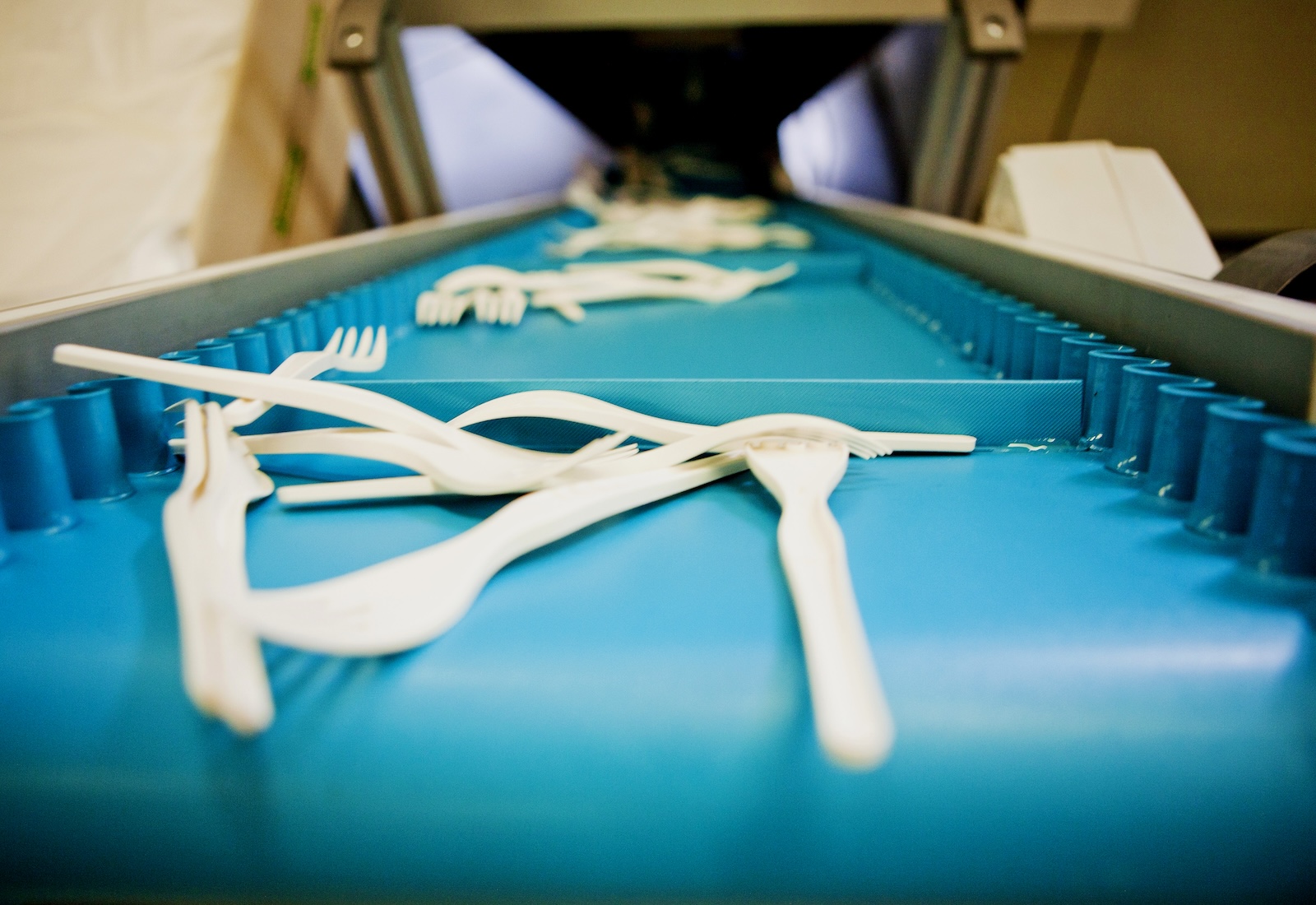 Compostable utensils travel down a blue conveyor belt away from the camera.