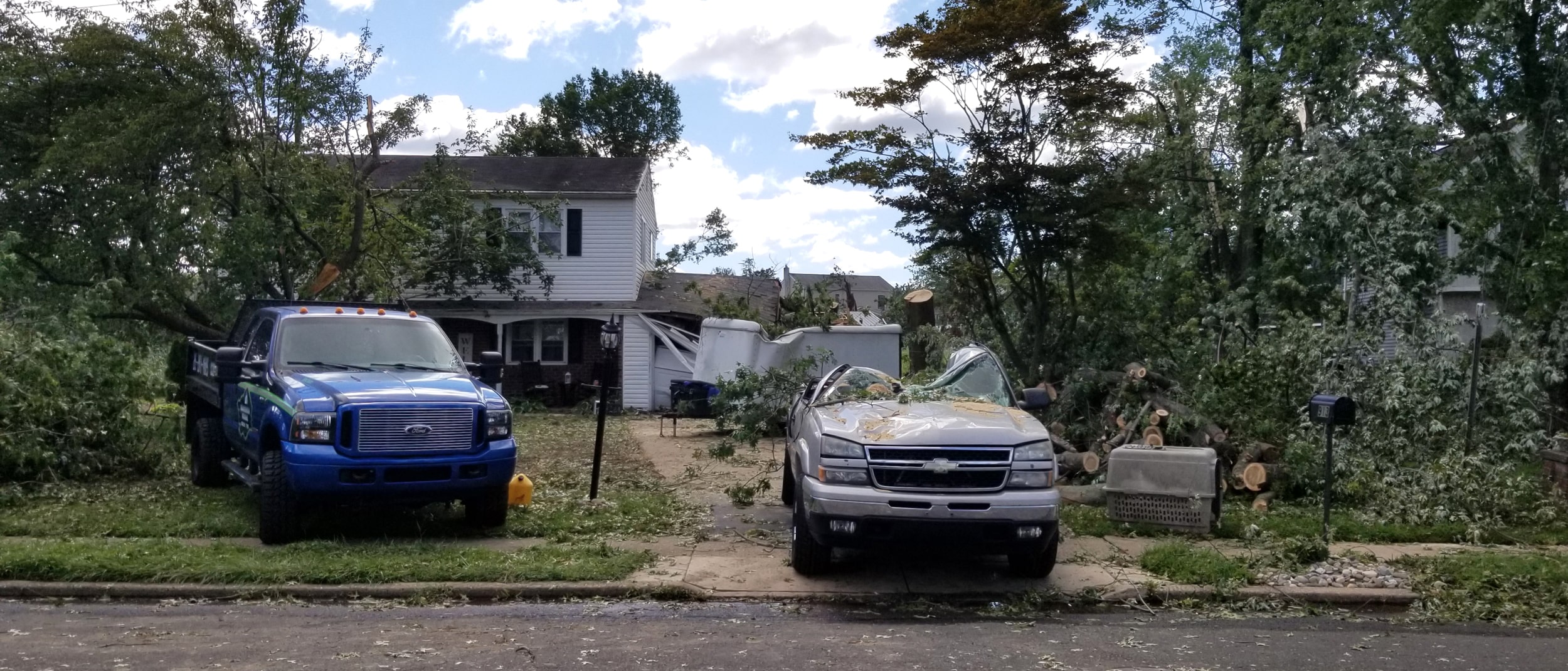 Downed trees and branches are scattered in front of a home and a truck is crushed in from one of the trees