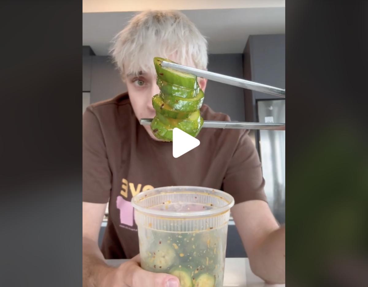 A screengrab of Logan Moffitt showing a bite of cucumber salad between two chopsticks, with a play button over the image