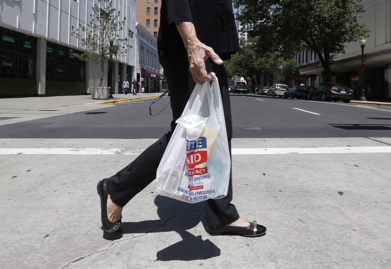 Cropped view of a shopper dressed in black, walking while holding a Rite Aid-branded plastic bag.