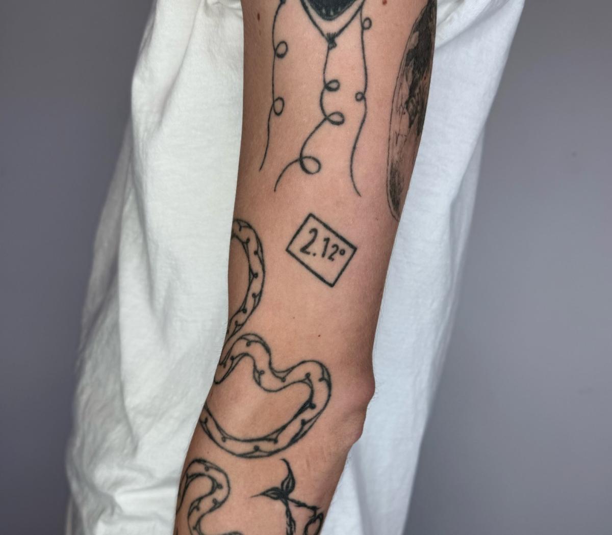 A photo of an arm with many tattoos, including the number 2.12 in a box