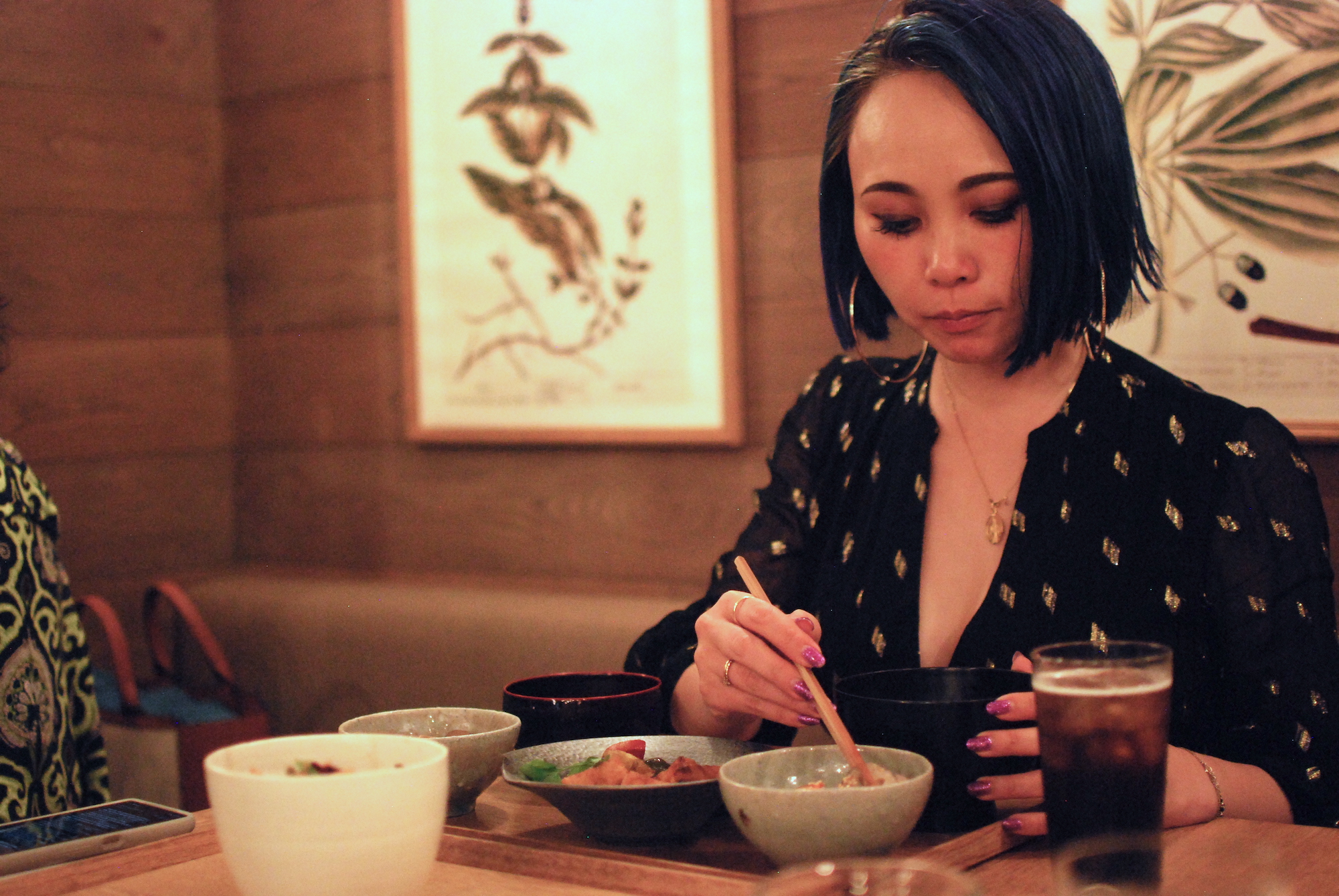 A woman uses chopsticks to pick food up from a bowl in a restaurant