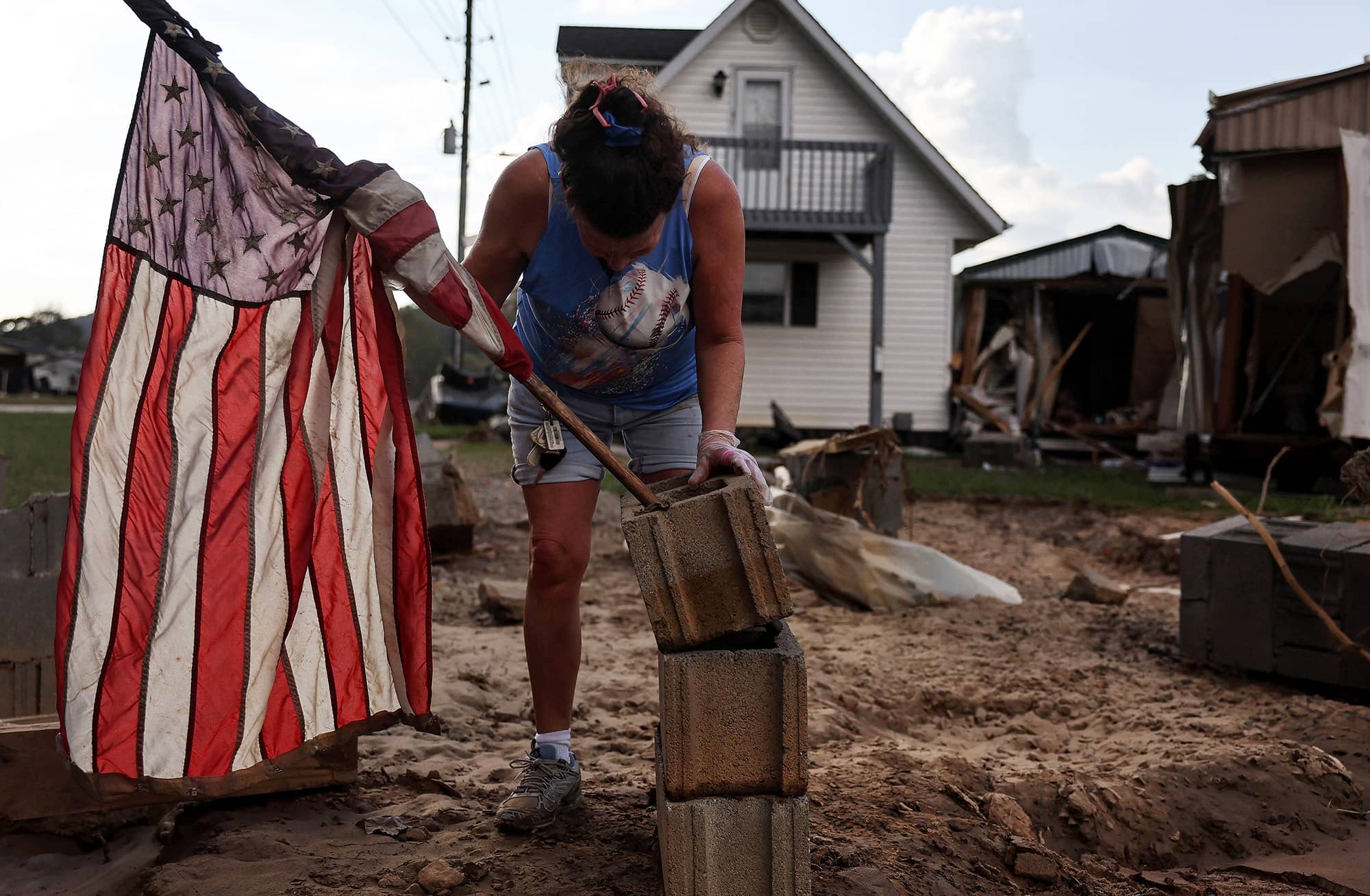 A woman mounts an American flag to a stack of cinderblocks outside her friend’s destroyed mobile home (at right) in the aftermath of Hurricane Helene flooding in Swannanoa, North Carolina.