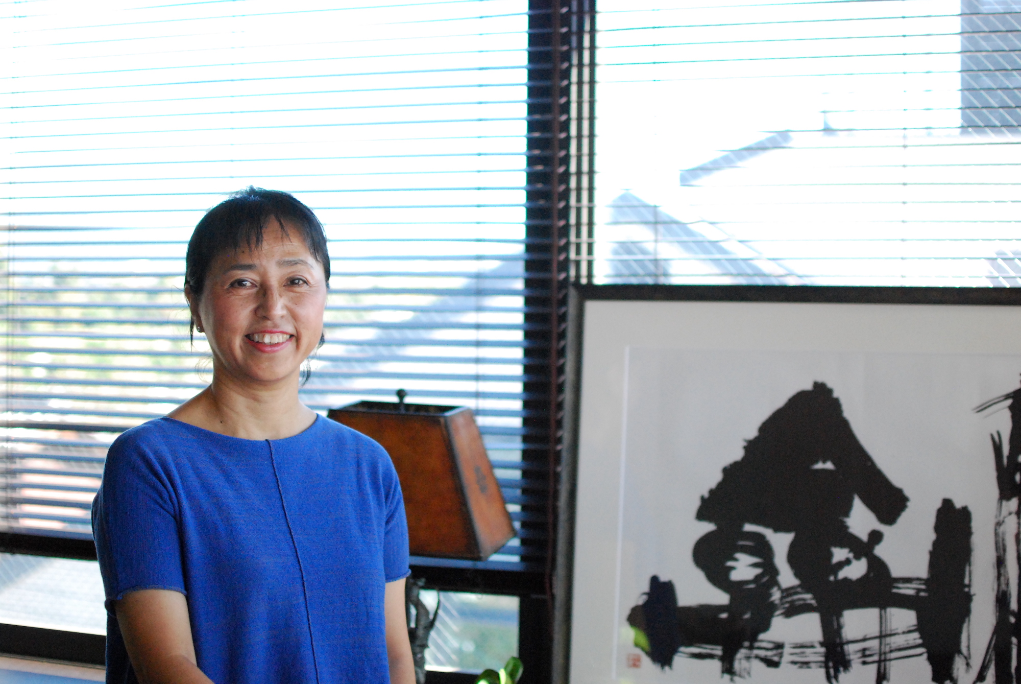 A woman in a blue shirt poses for a photo in an apartment next to a large piece of art