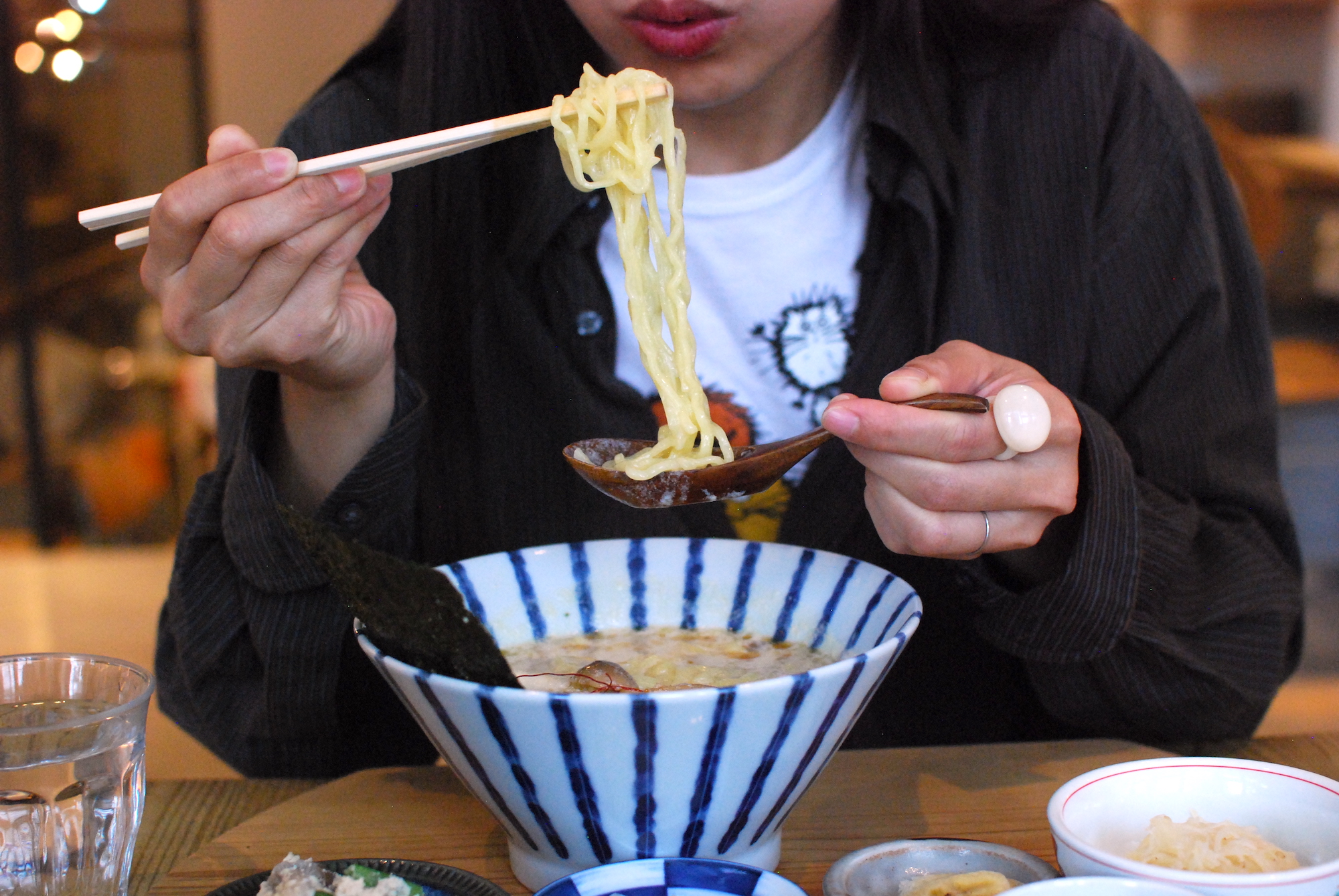 a person eats a bowl of vegan ramen with chopsticks and a spoon