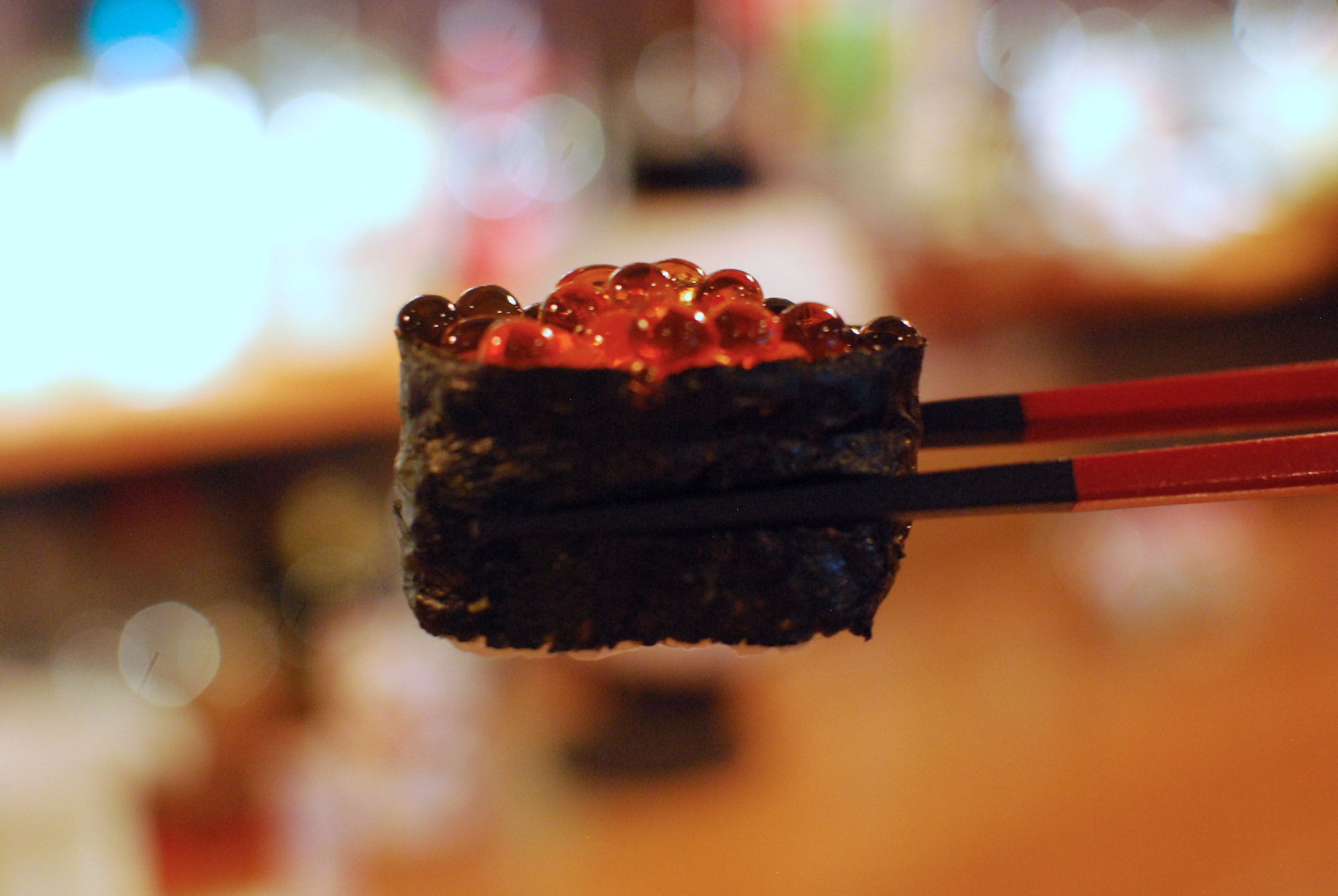 A closeup of a piece of vegan sushi held by chopsticks