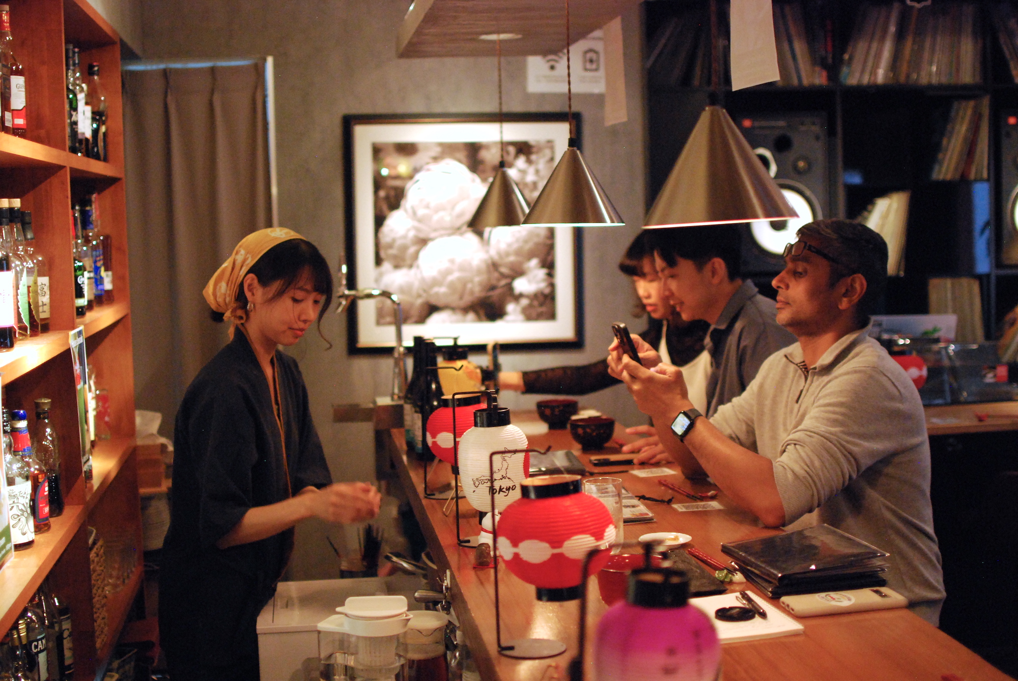 A woman with a bandana tied around her hair stands behind a busy bar